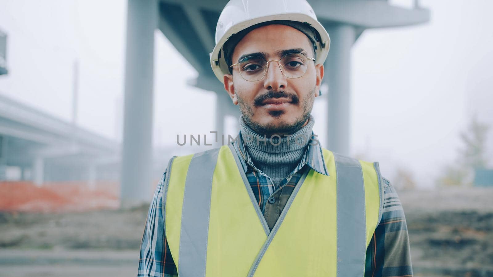 Portrait of Middle Eastern builder wearing uniform standing outdoors in building site and looking at camera. Profession and specialists concept.