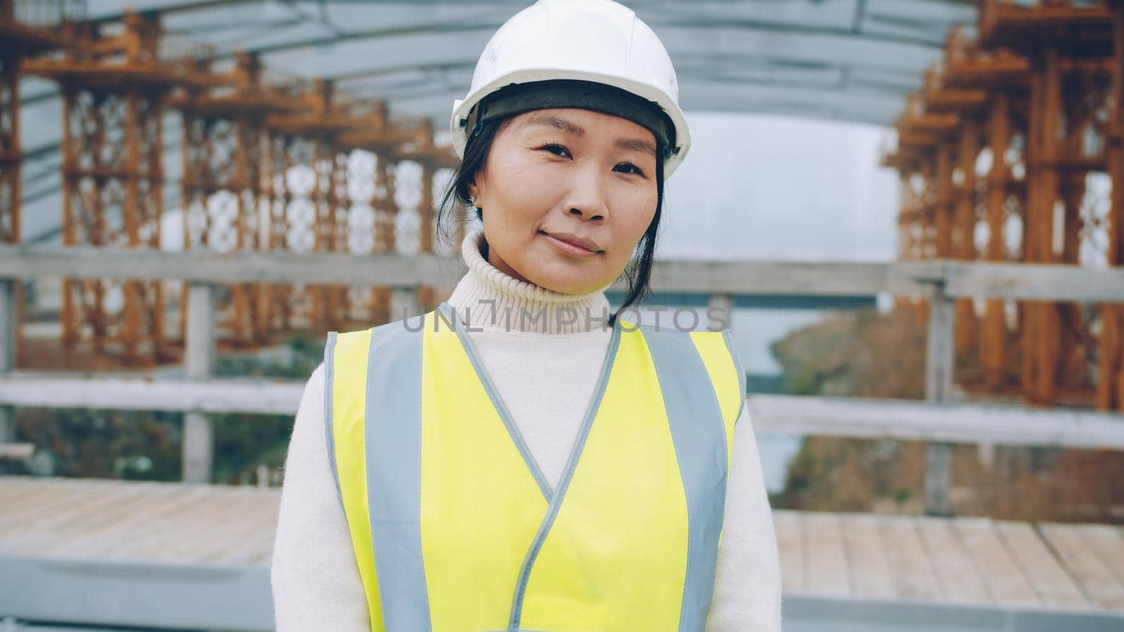 portrait of female builder standing outside construction area wearing safety helmet by silverkblack