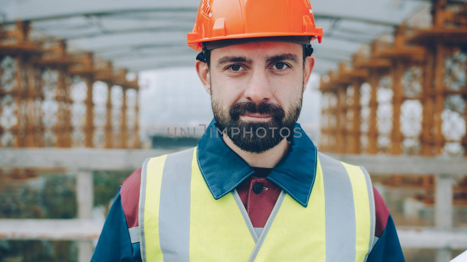 Portrait of confident construction workman wearing safety uniform standing in building area by silverkblack