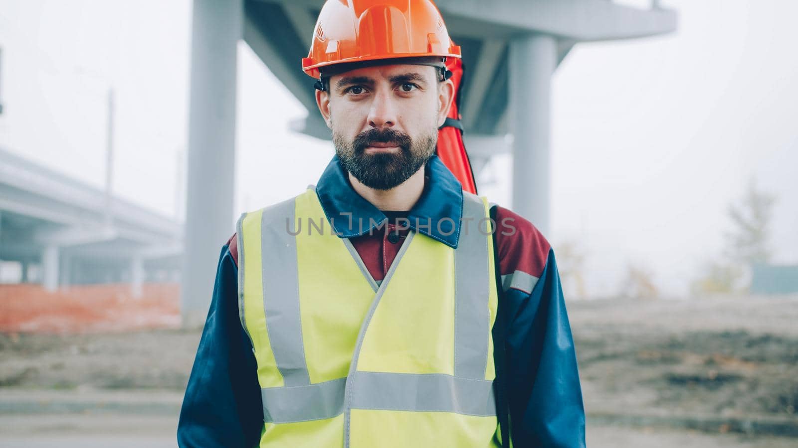 portrait of serious surveyor standing in building area with theodolite in background by silverkblack