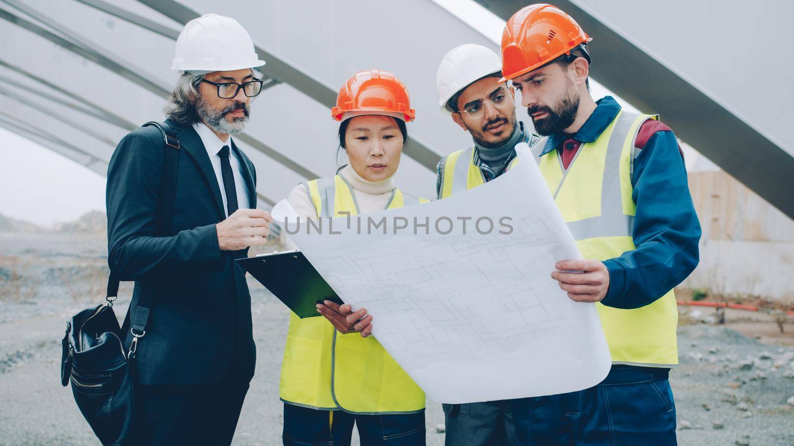 Construction workers are discussing project with manager standing in building area reading papers and looking around. People and occupation concept.