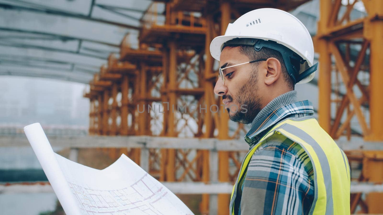 Portrait of engineer planning work at construction site looking at blueprint outdoors by silverkblack