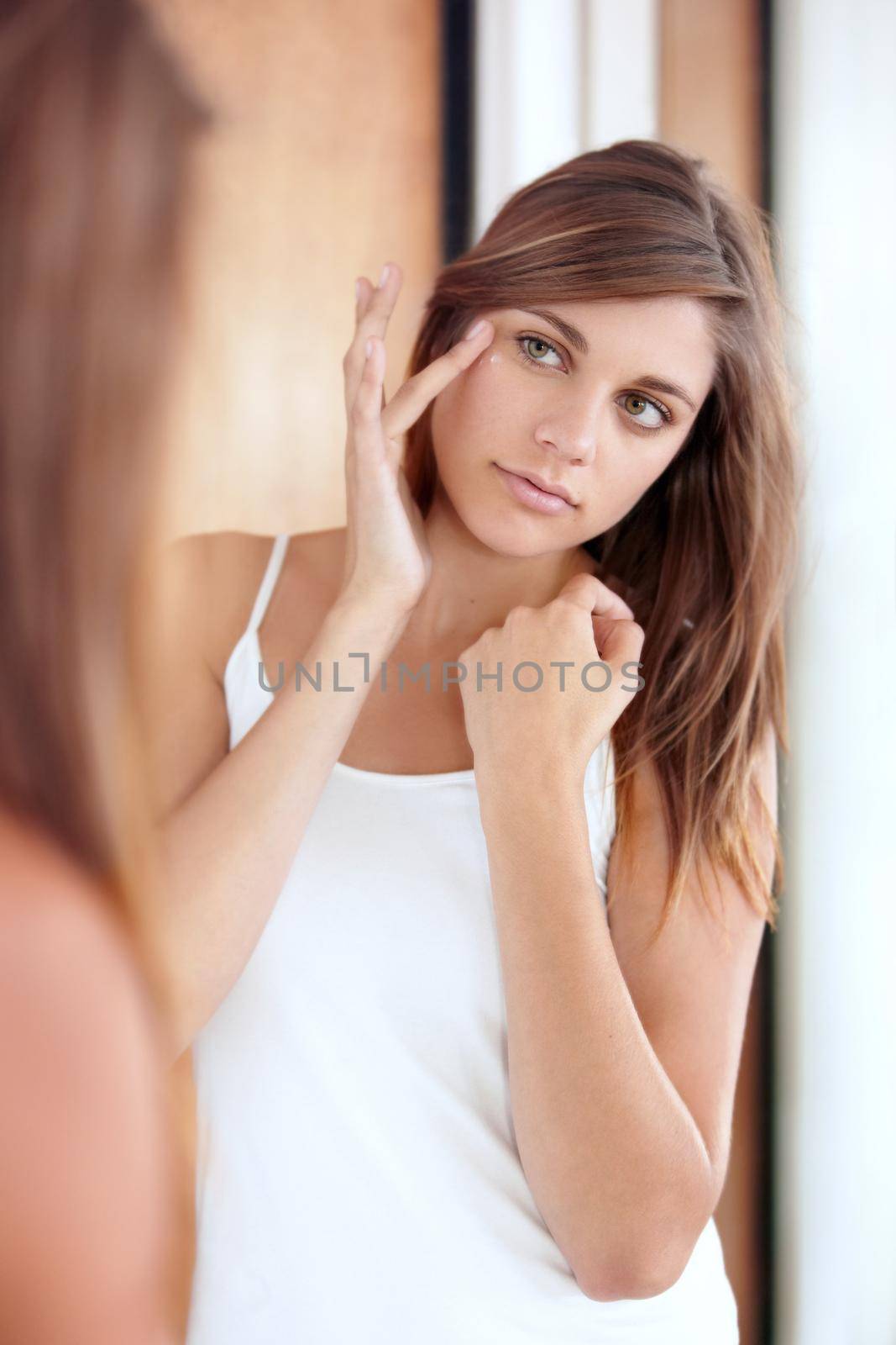 Preventing wrinkles before they start. A beautiful young woman applying cream to her face. by YuriArcurs