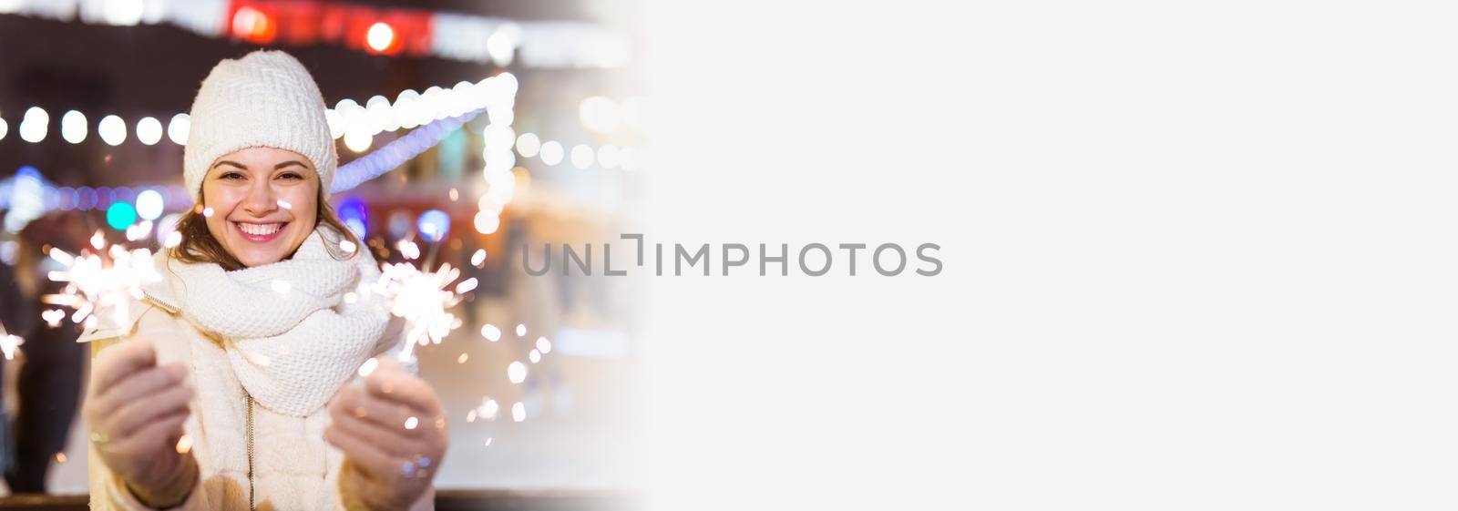 Young beautiful woman in knitted hat and scarf standing in the city with bengal light, sparkler. Concept celebration and christmas