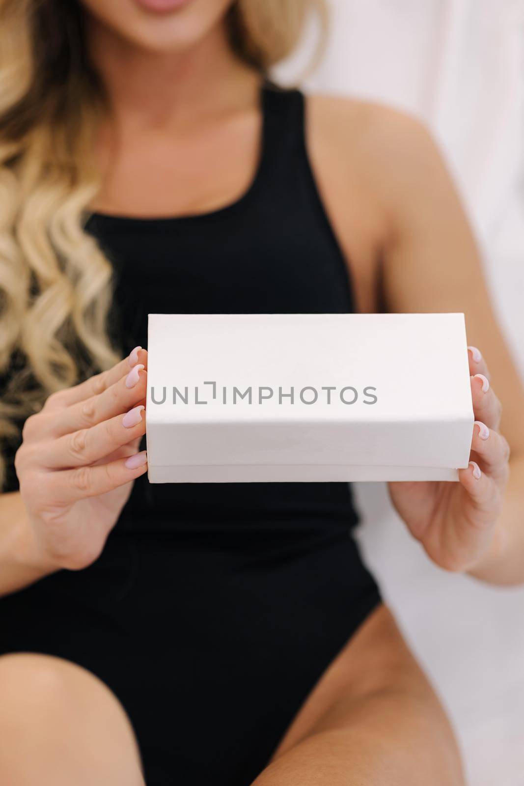 Beautiful female model in cosmetology studio hold white box in a hand. Sexy woman in black bodysuit. Advertising of beauty product. Middle selection by Gritsiv