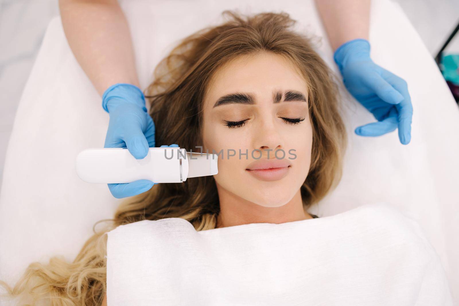 Close up of female face with soft skin. Woman at cosmetology clinic taking a beauty procedure for skin. Beautician using peeling device, ultrasonic clining. Gorgeous woman by Gritsiv