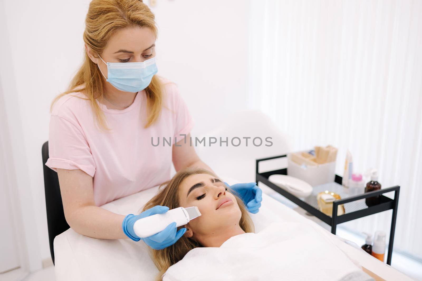 Female at cosmetic beauty spa clinic has facial hardware cosmetology. Woman making beauty procedures. Peeling device by Gritsiv