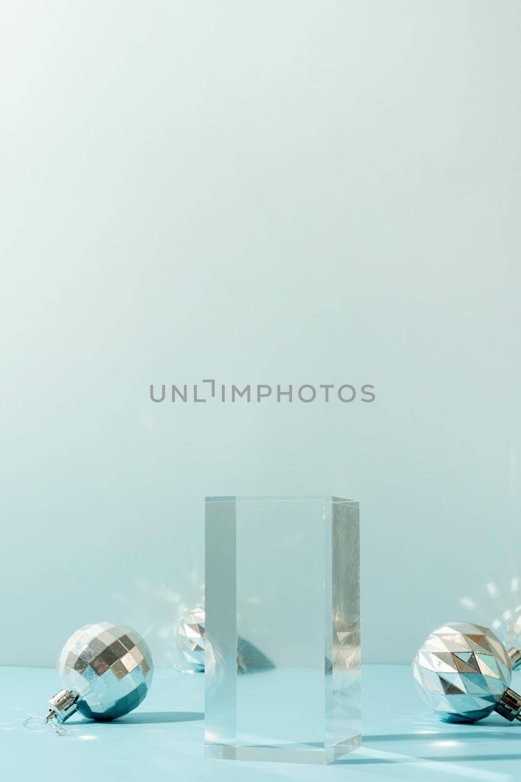 A minimalistic scene of glass podium with christmas decorative balls on a light blue background. Catwalk for the presentation of products and cosmetics. Showcase with a stage for products, mockup design, seasonal