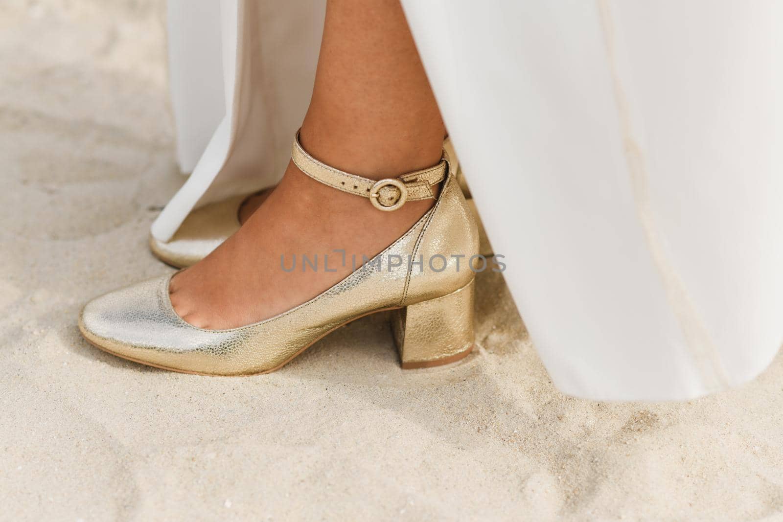 The golden shiny shoes of the bride on white sand on the ocean coast