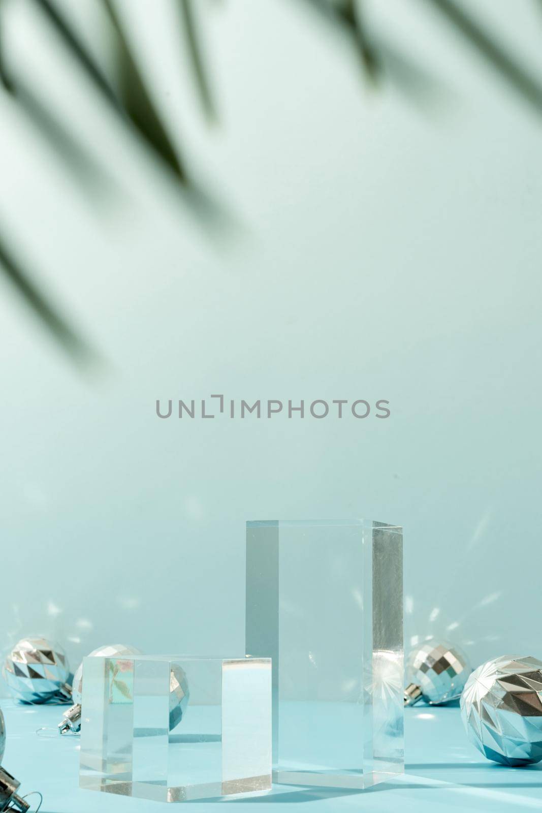 A minimalistic scene of glass podium with christmas decorative balls and pine tree on a light blue background by Desperada