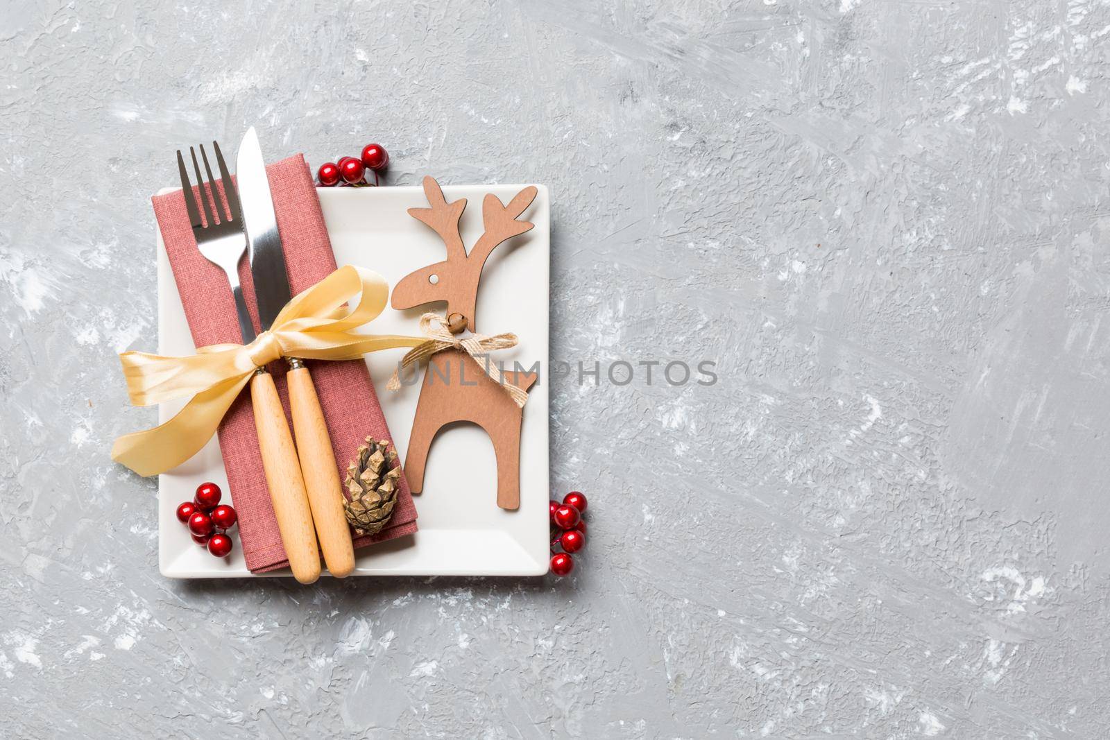 Top view of holiday dinner decorated with dried fruit and cinnamon on cement background. Set of plate, urensil and New Year decorations. Christmas time concept with epmty space for your design.