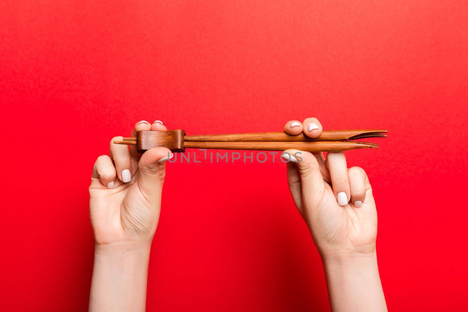 Crop image of two female hands holding chopsticks on red background. Ready to eat concept with copy space.