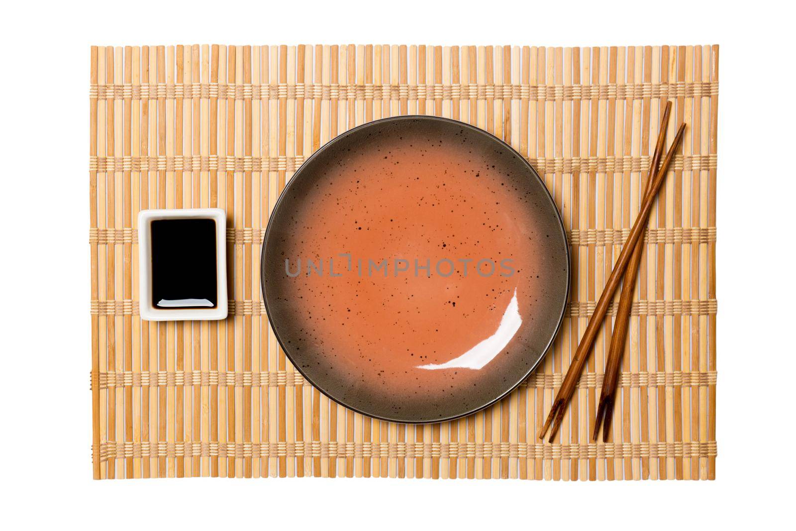 Empty round brown plate with chopsticks for sushi and soy sauce on yellow bamboo mat background. Top view with copy space for you design.