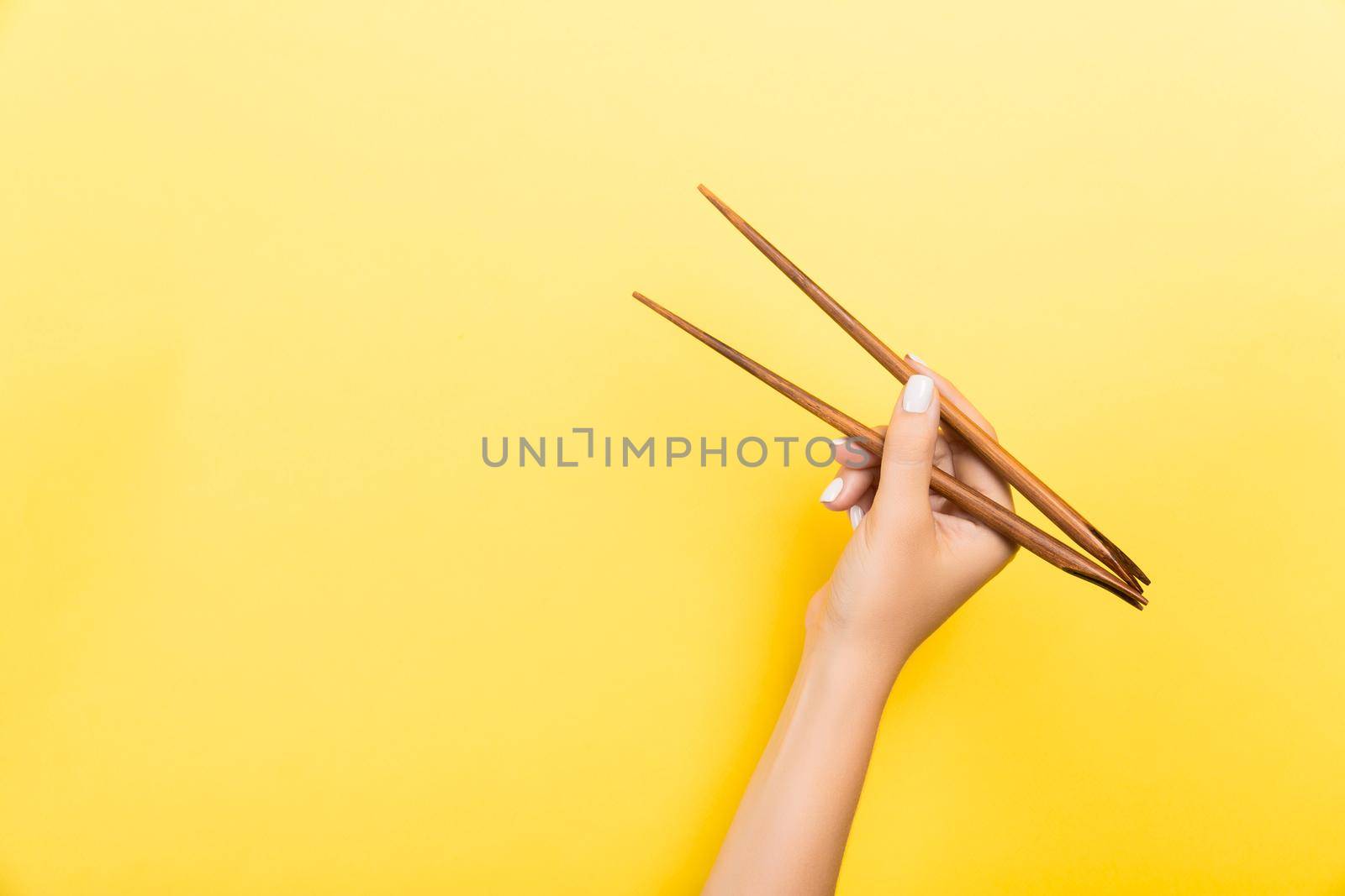 Female hand with chopsticks on yellow background. Traditional asian food with emty space for your design.