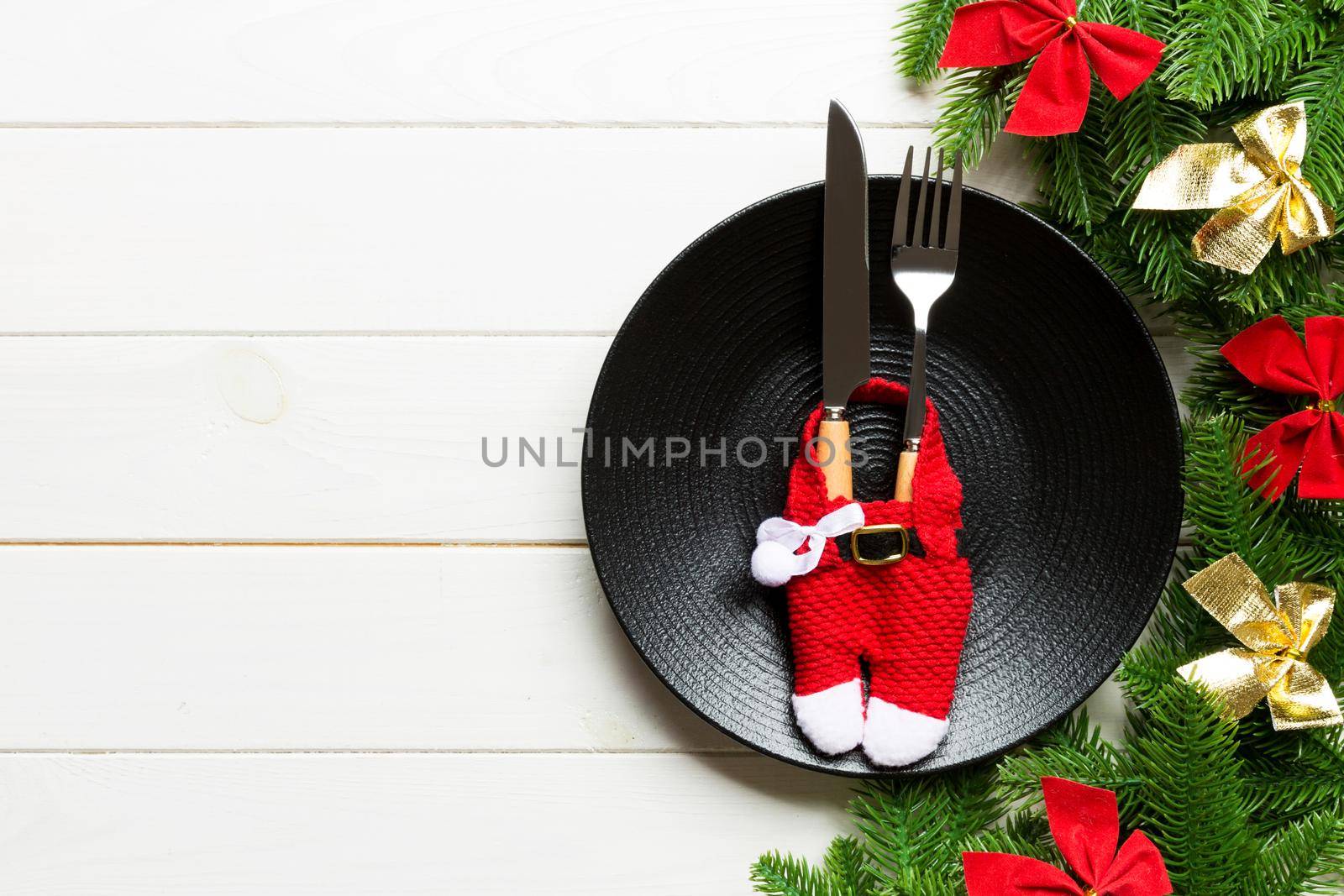 Holiday composition of plate and flatware decorated with Santa clothes on wooden background. Top view of Christmas decorations. Festive time concept.