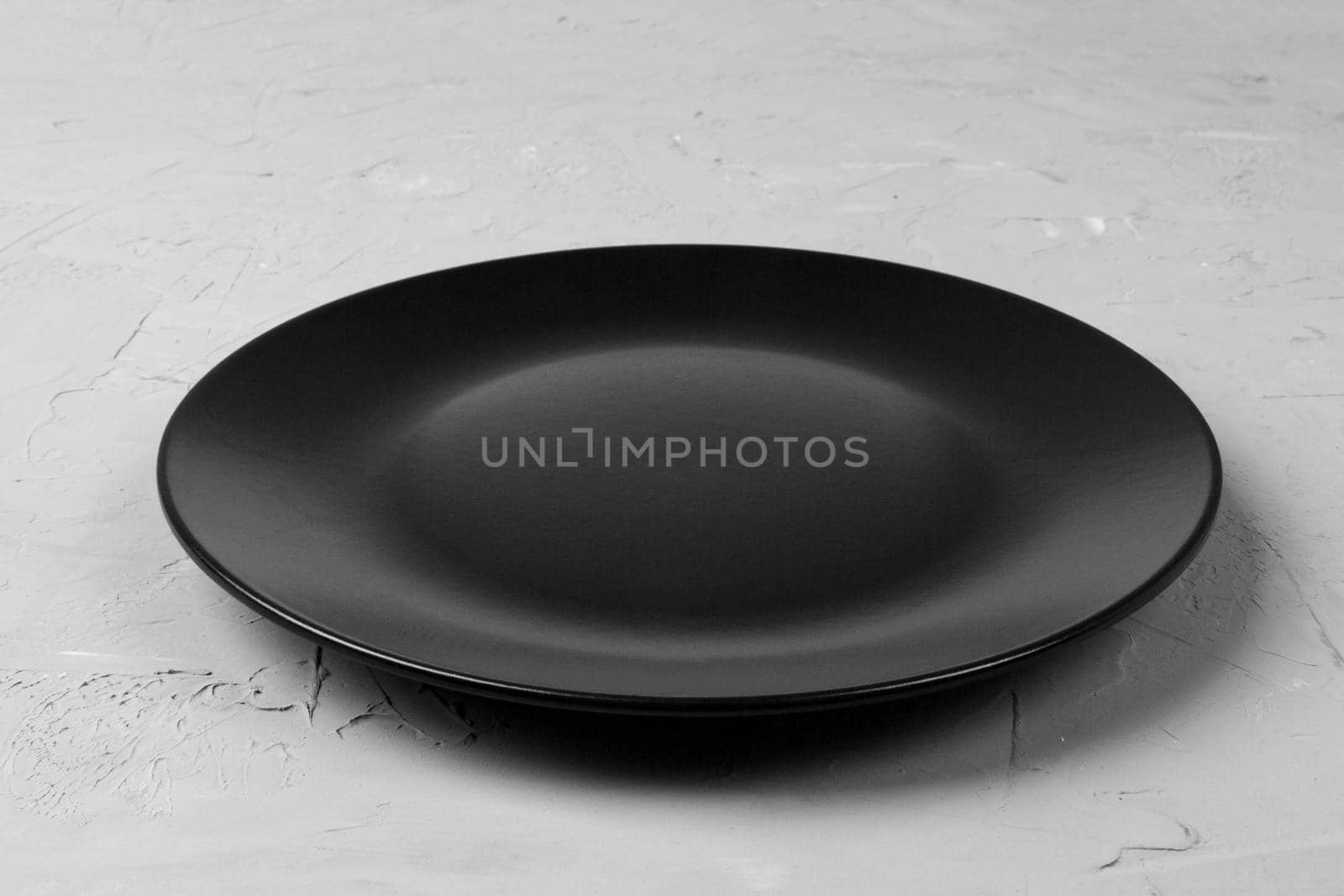 Top view of matte round empty black plate on grey cement background copy space for you design. Perspective view.