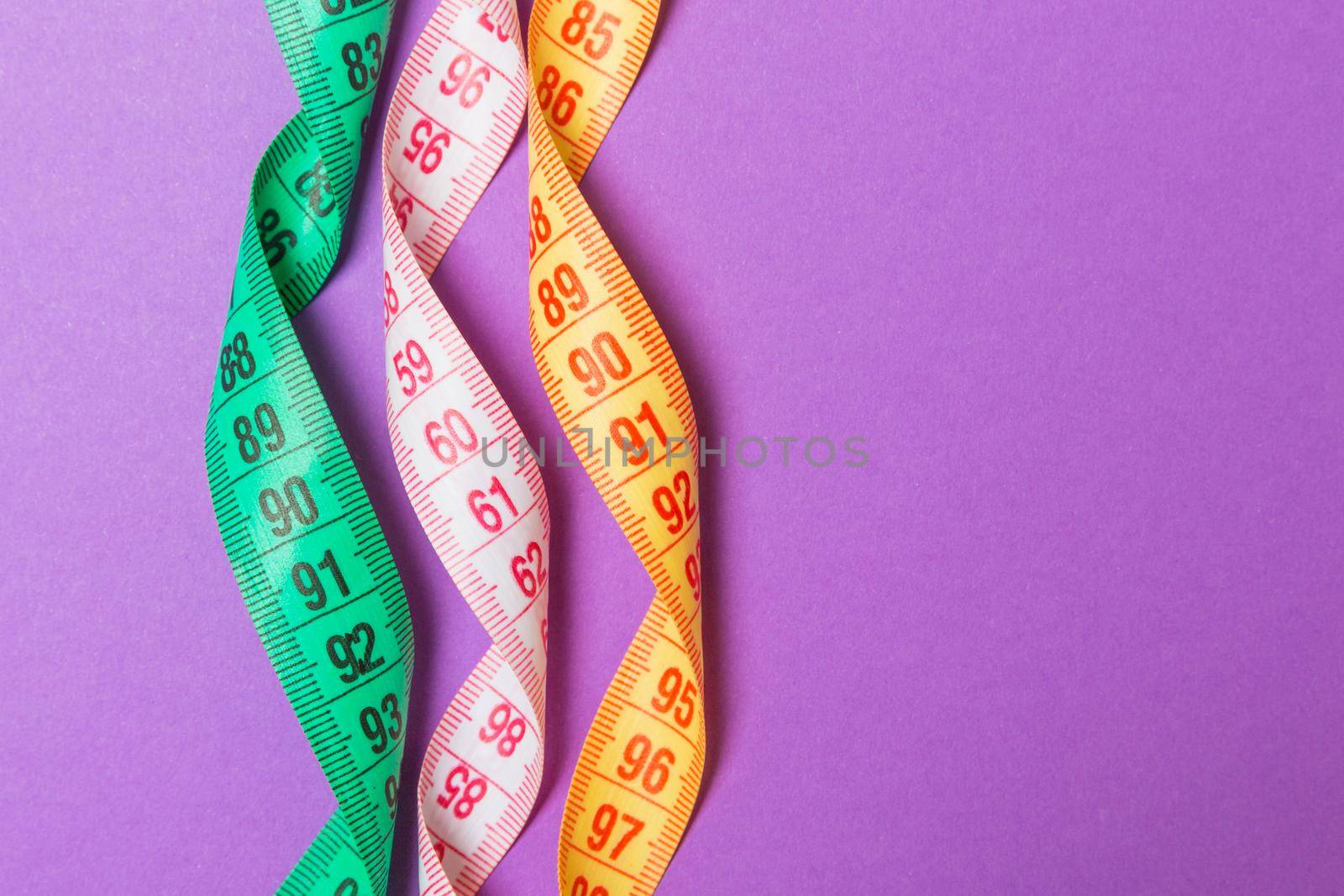 Close up of colorful measure tapes on purple background. Perfect female figure measurements concept.