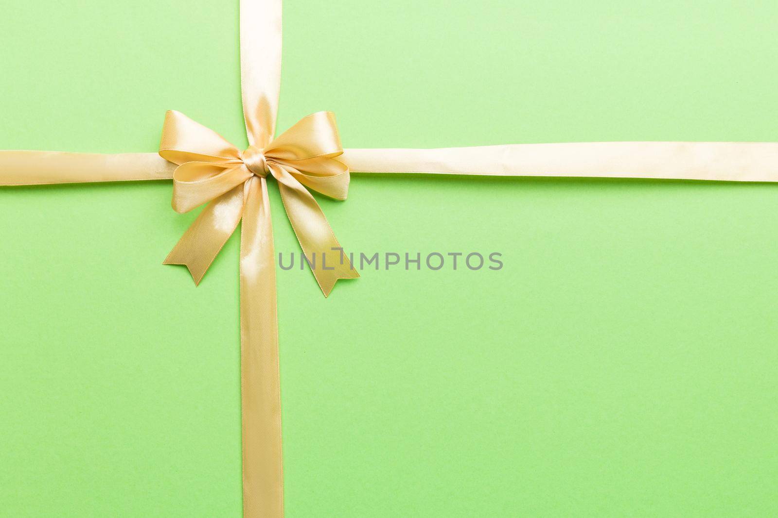 Top view of gold ribbon rolled and yellowbow isolated on colored background. Flat lay with copy space.