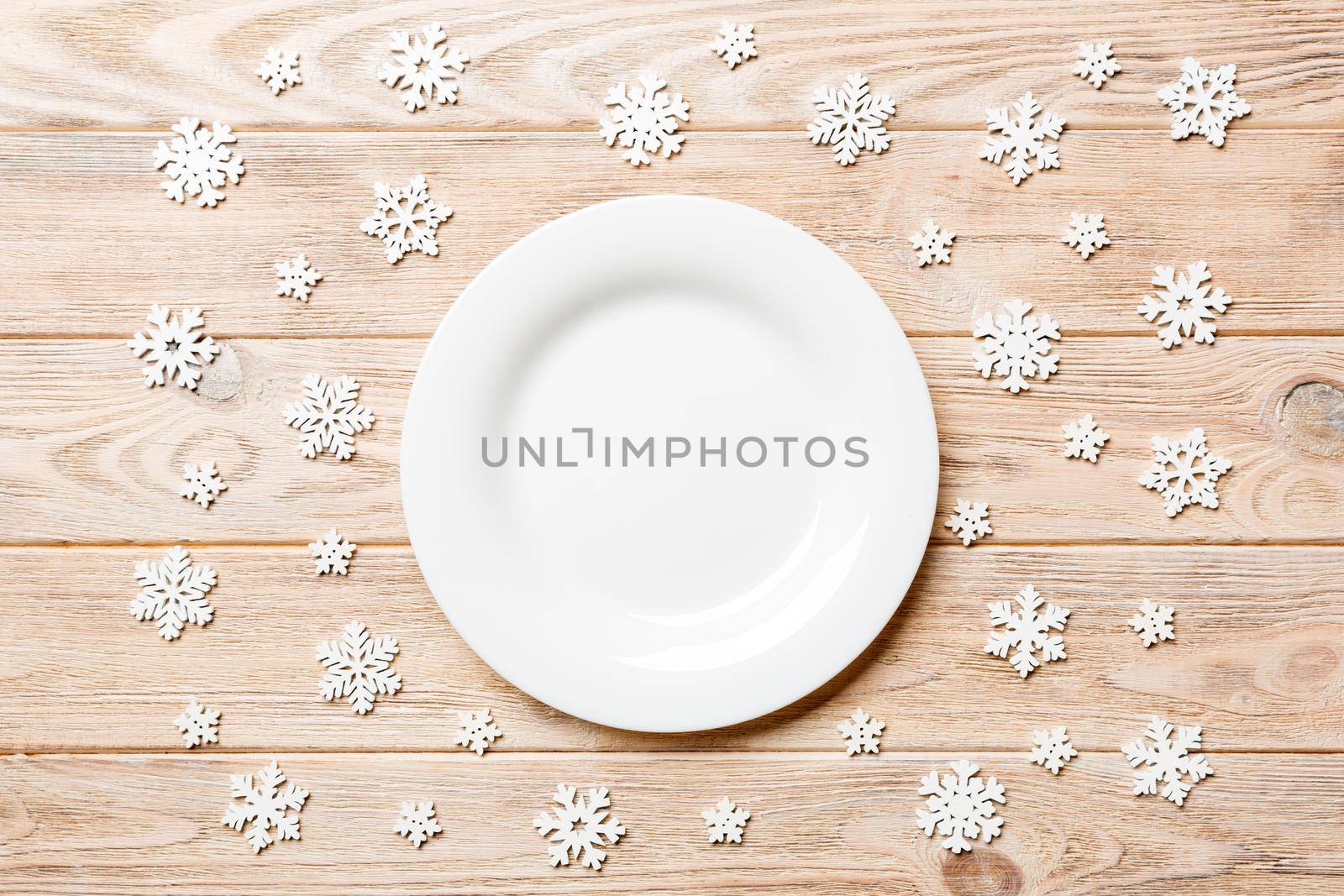 Top view of empty plate surrounded with snowflakes on wooden background. New Year dinner concept.