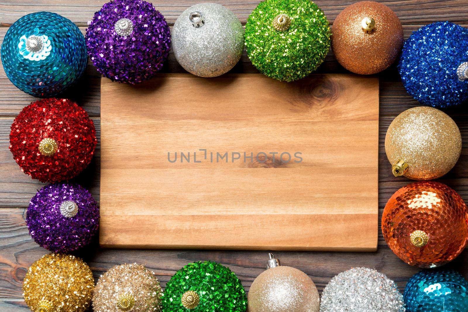 Top view of empty plate surrounded with colorful baubles on wooden background. New Year decorations. Christmas Eve concept.