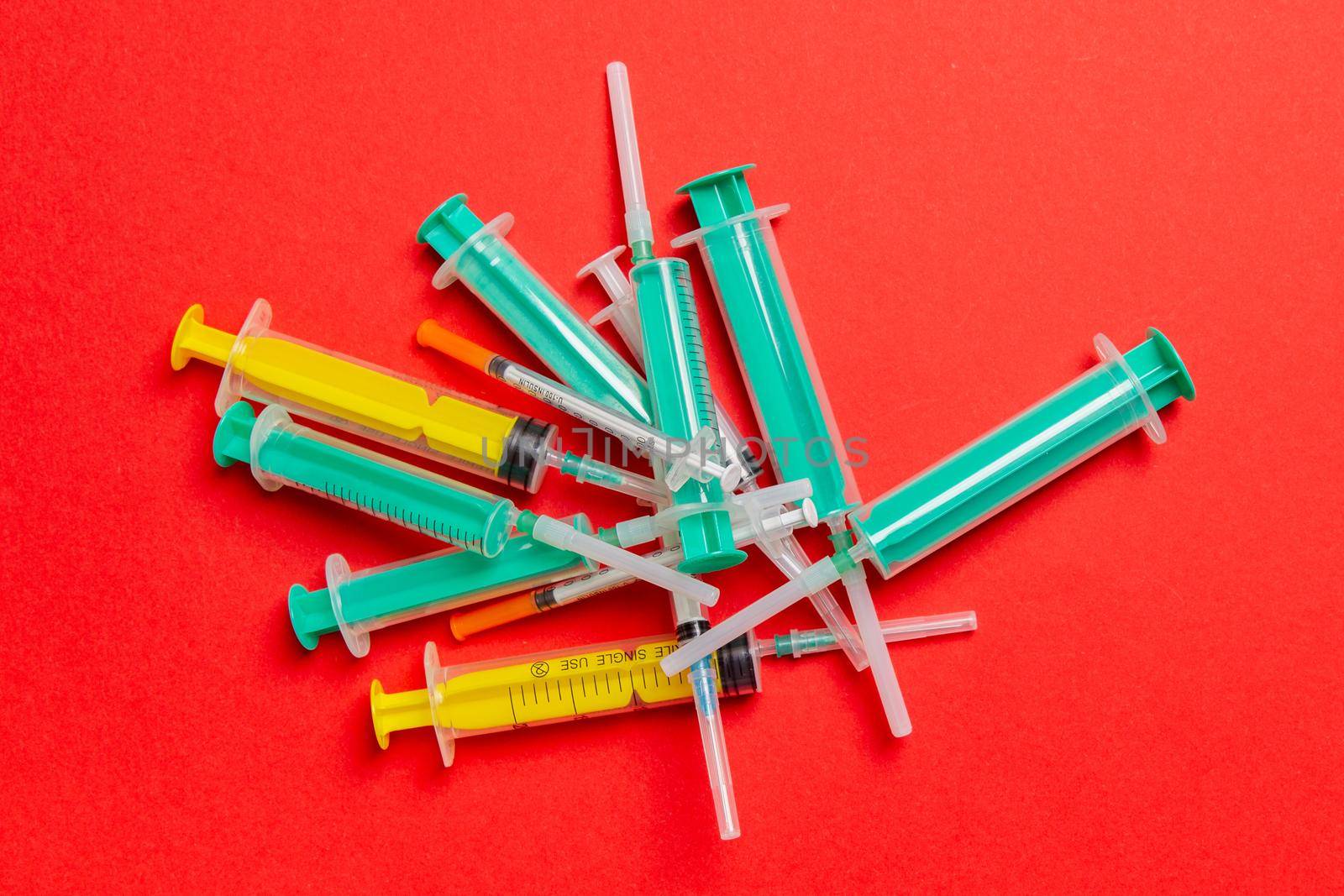 Top view of a pile of medical syringes and insulin syringes with needles at red background with copy space. Injection treatment concept.