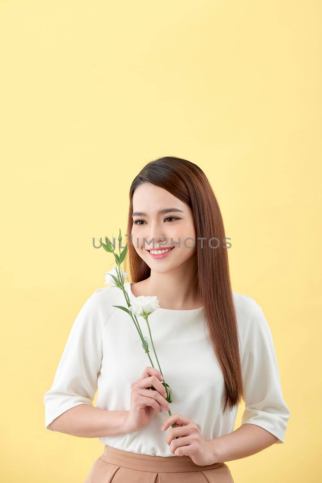 Beauty portrait of lady 20s holding white lisianthus flowers over yellow background