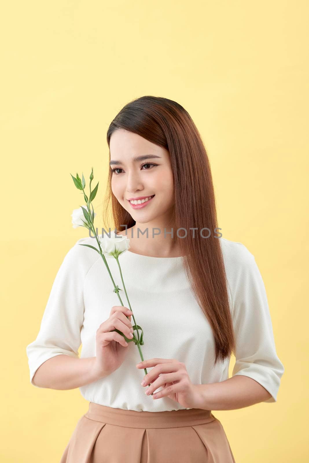 Beauty portrait of lady 20s holding white lisianthus flowers over yellow background by makidotvn