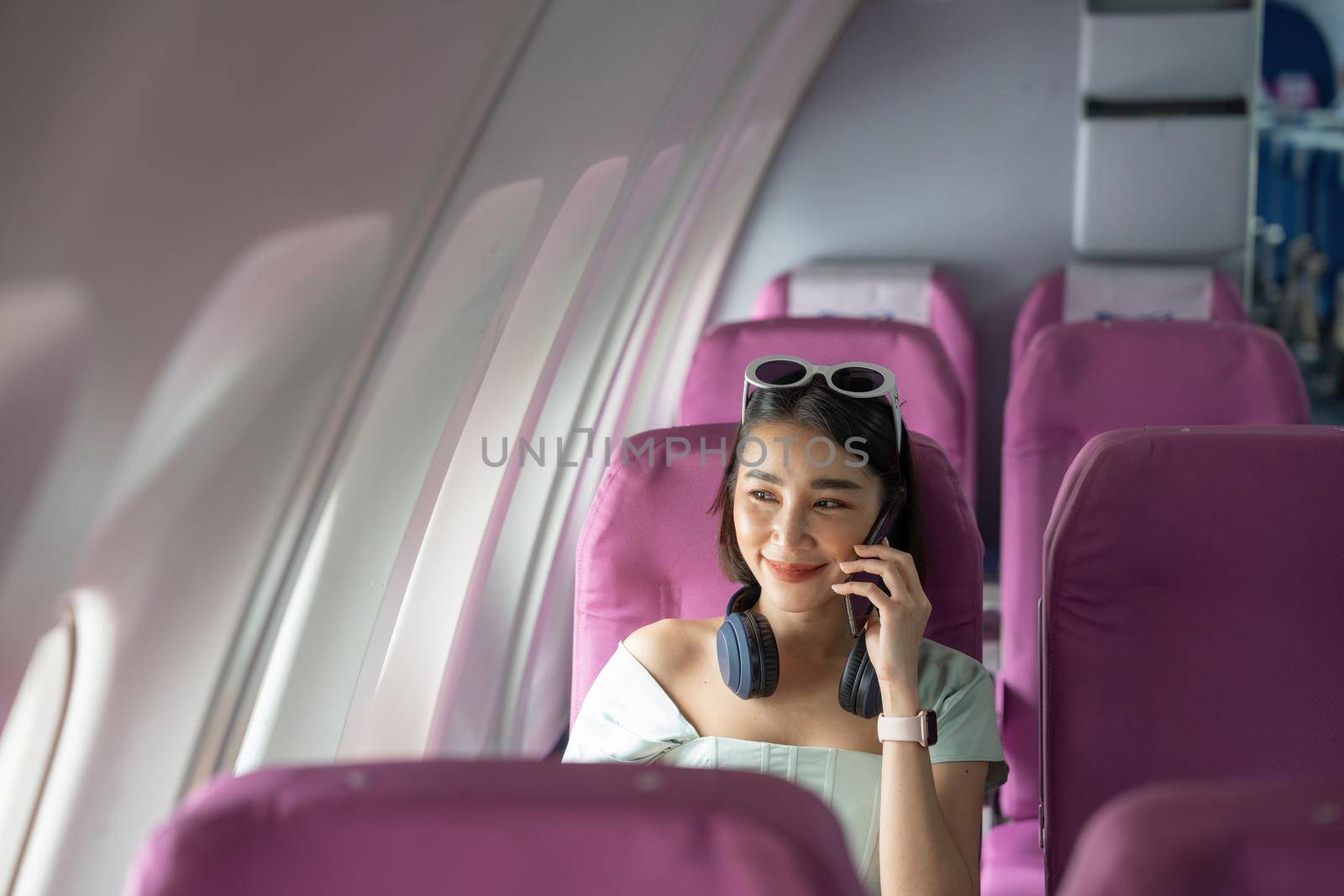 Attractive asian woman passenger of airplane calling mobile phone on board. tourism traveler concept. by nateemee