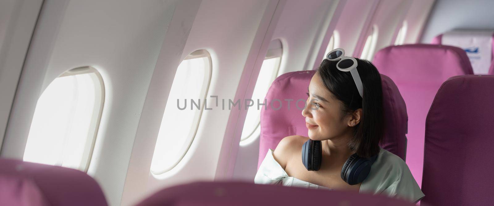 Happy young asian woman on passenger seat near window in airplane. alone travelling concept