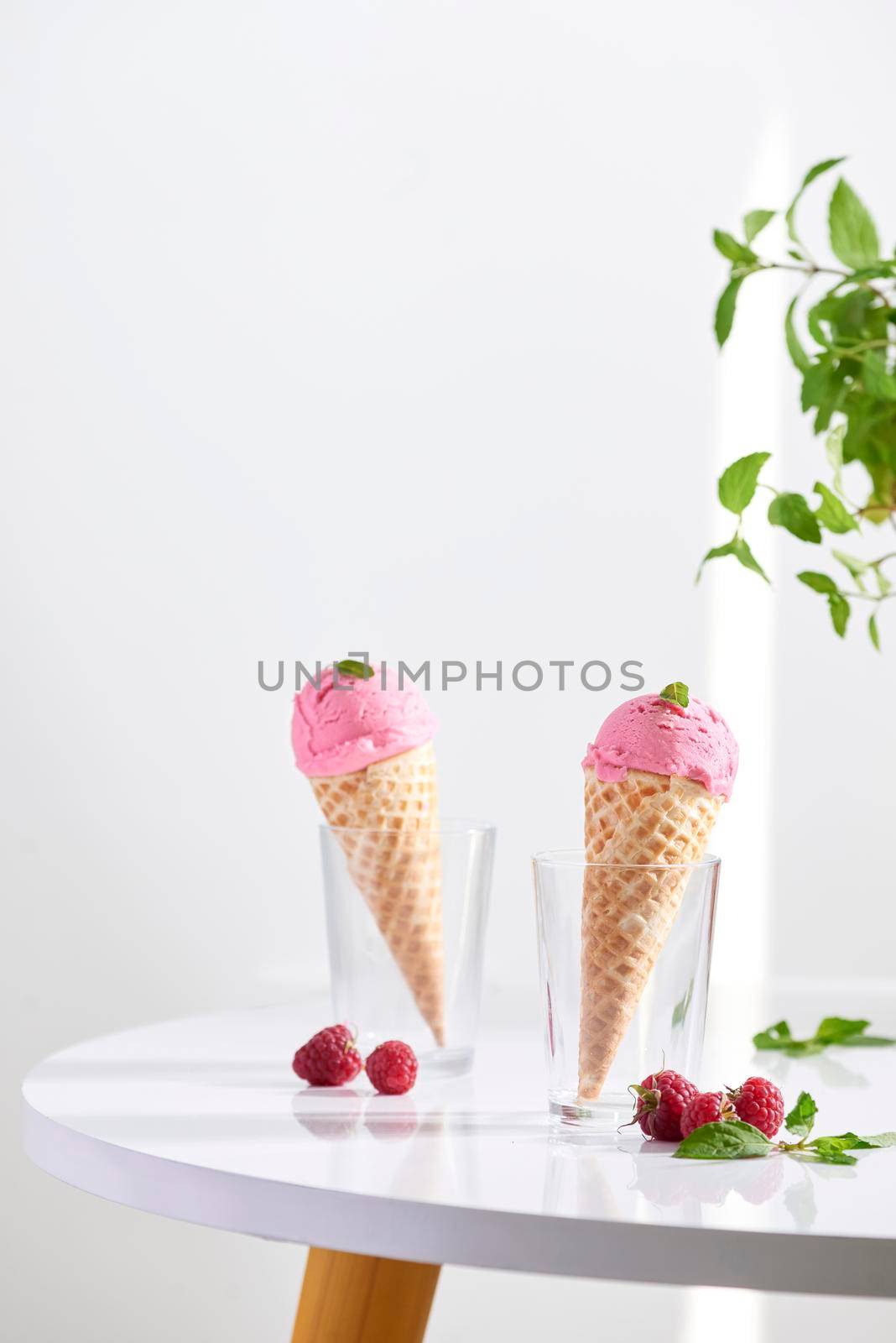 Waffle cone filled with fresh raspberry ice cream in glass cup with fresh raspberry sitting on tabletop