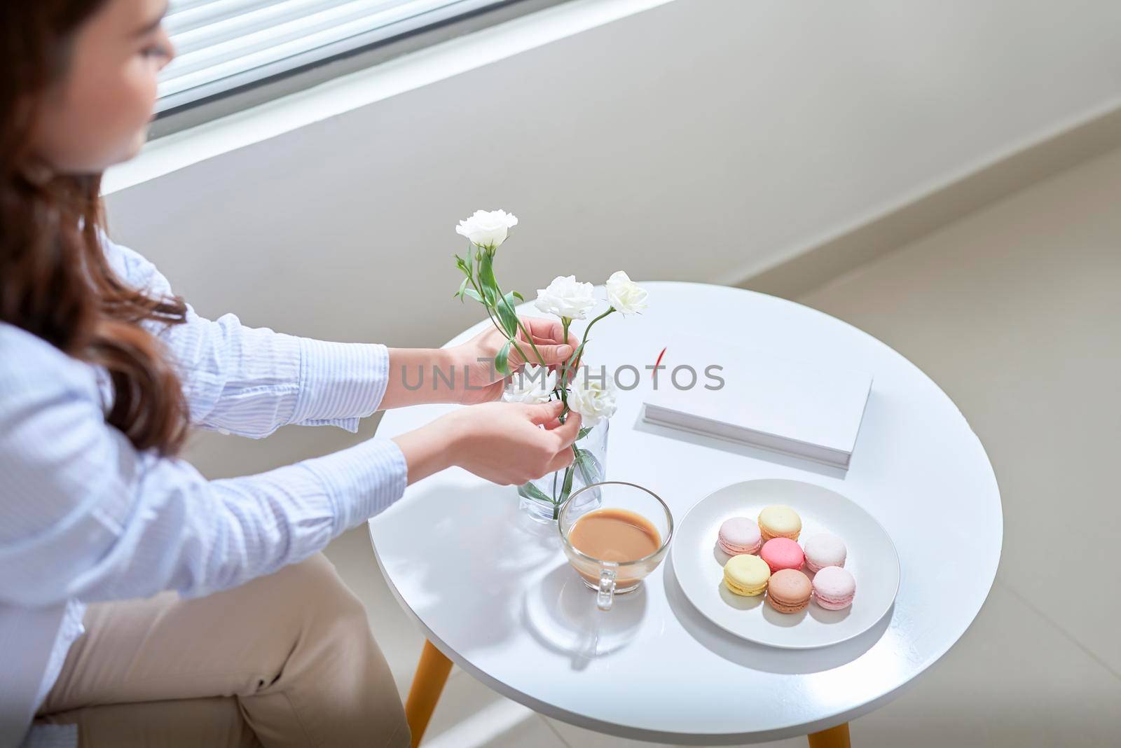 Woman arranging lisianthus flowers in a glass vase at home. 