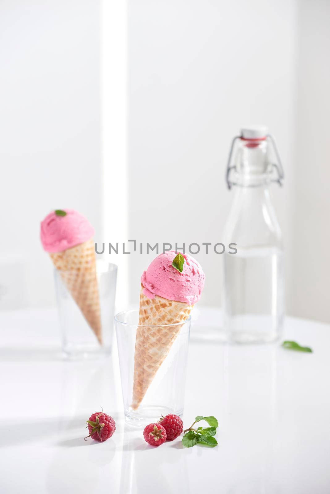 Waffle cone filled with fresh raspberry ice cream in glass cup with fresh raspberry sitting on tabletop