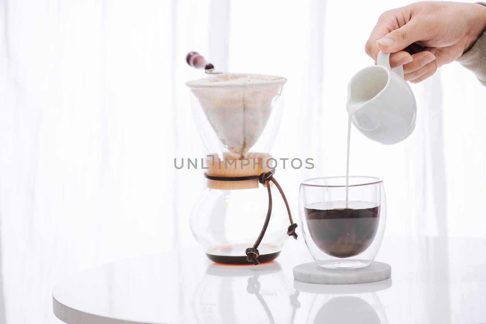 Man pouring milk into glass with cold brew coffee on table