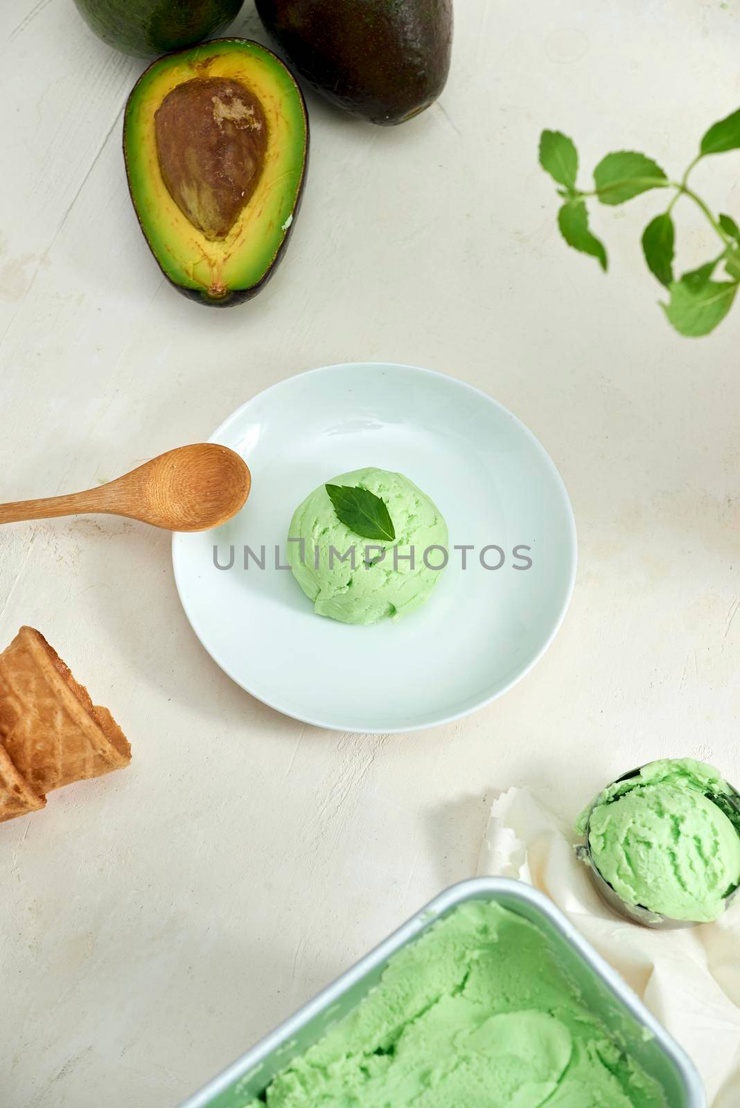 Avocado ice cream balls on a white plate, a spoon on a white background.