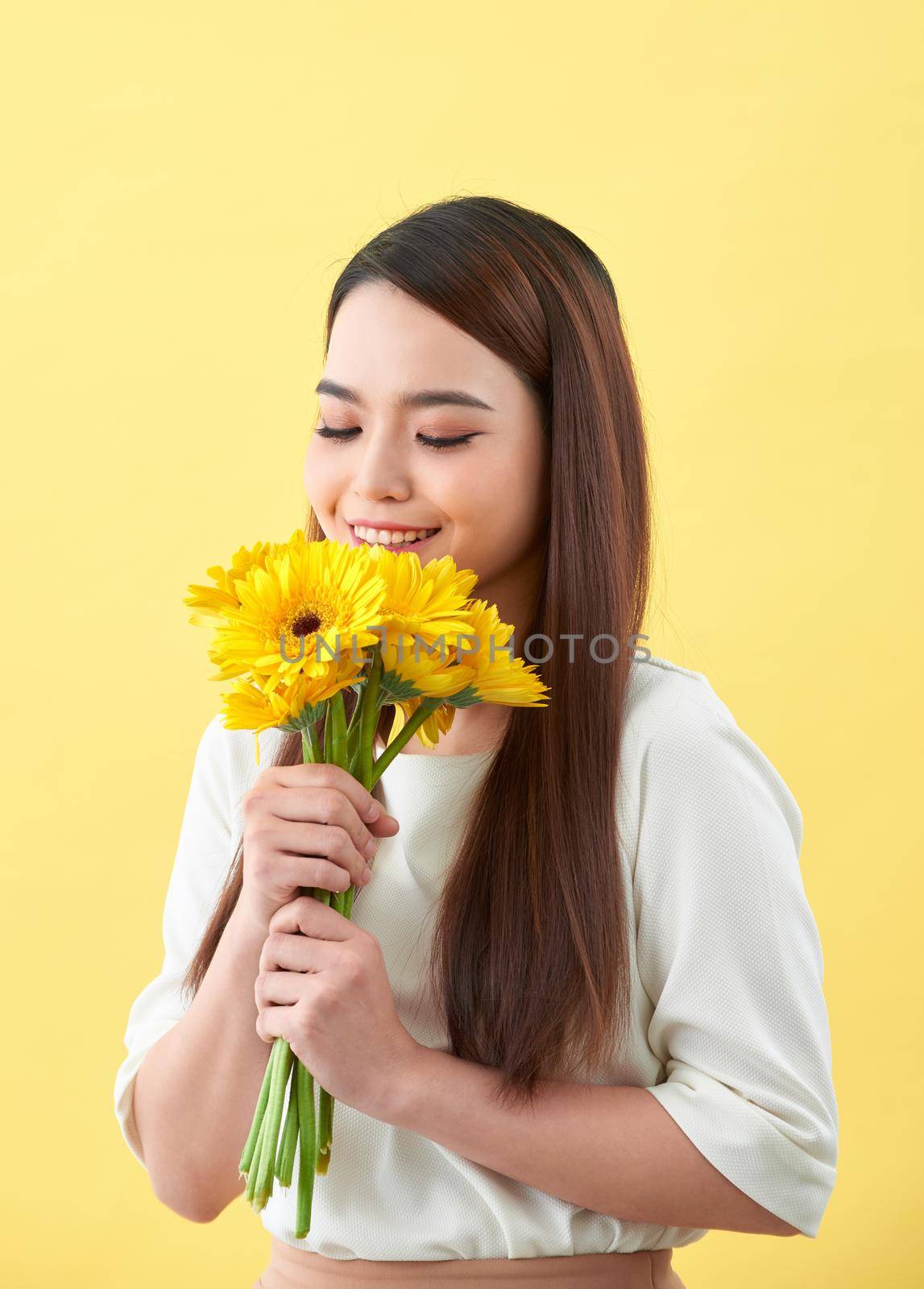 young woman smelling sunflowers on the yellow background by makidotvn