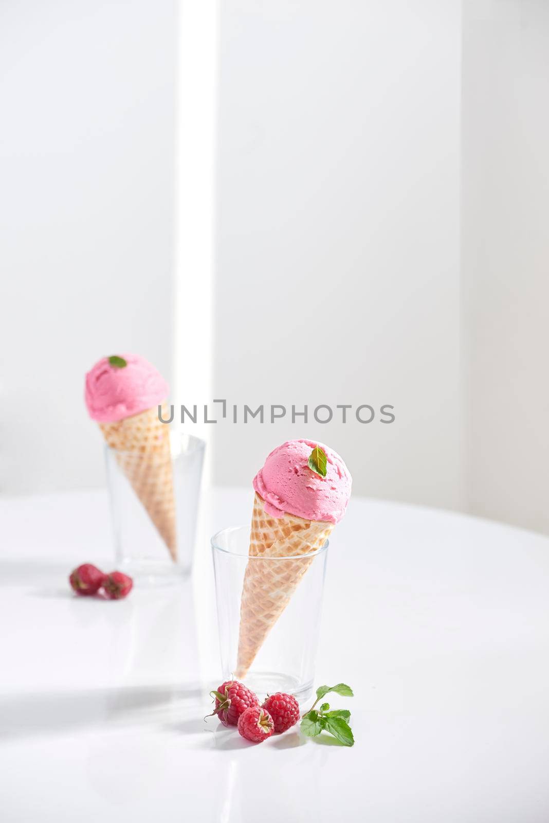 Waffle cone filled with fresh raspberry ice cream in glass cup with fresh raspberry sitting on tabletop by makidotvn