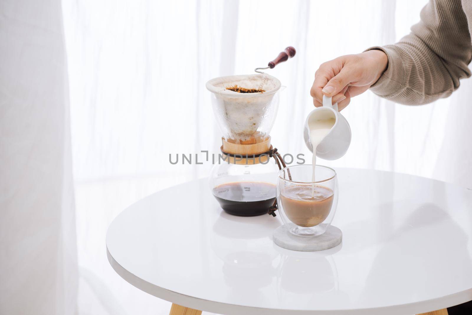 Man pouring milk into glass with cold brew coffee on table