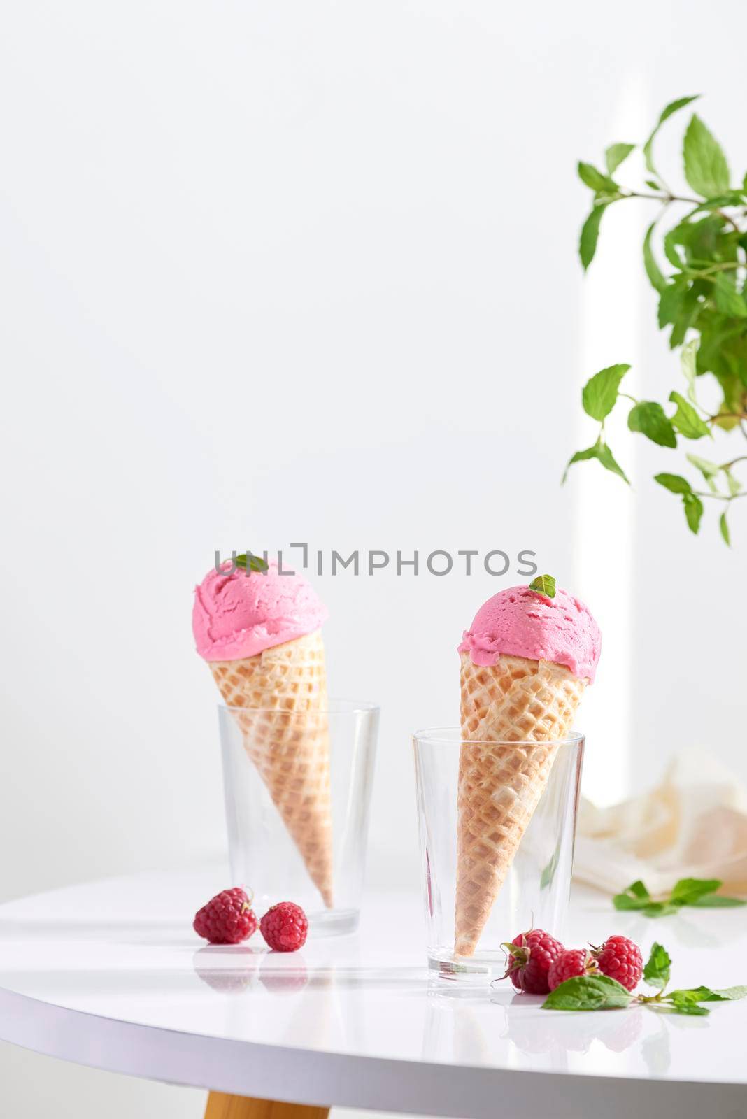 Waffle cone filled with fresh raspberry ice cream in glass cup with fresh raspberry sitting on tabletop by makidotvn