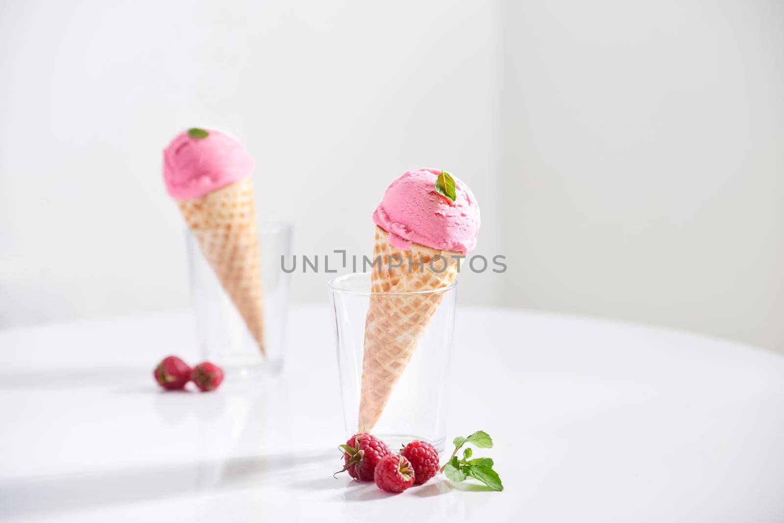 Waffle cone filled with fresh raspberry ice cream in glass cup with fresh raspberry sitting on tabletop by makidotvn