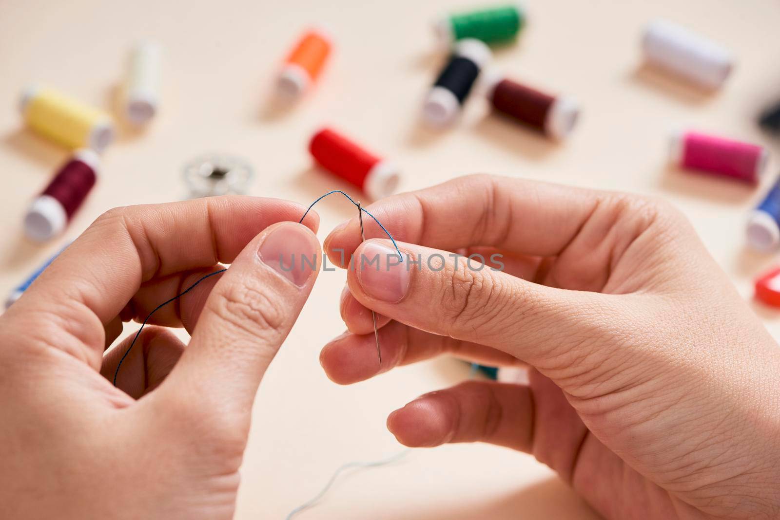 people, needlework, sewing and tailoring concept - tailor woman with thread in needle stitching fabric. Hands sewing with a needle and thread. Fingers pulling thread into the needle by makidotvn