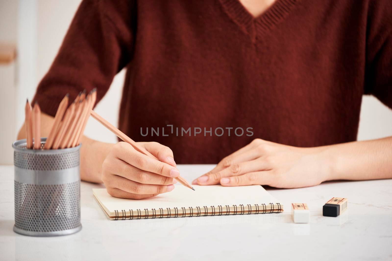 Hand with color pencils and blank sheet of paper on white table