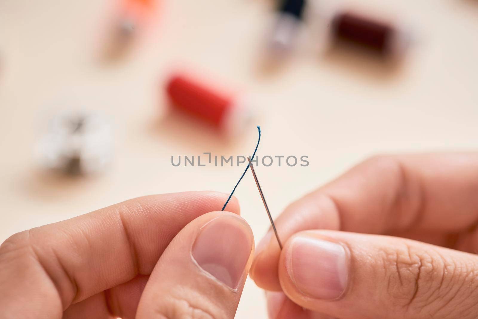 people, needlework, sewing and tailoring concept - tailor woman with thread in needle stitching fabric. Hands sewing with a needle and thread. Fingers pulling thread into the needle