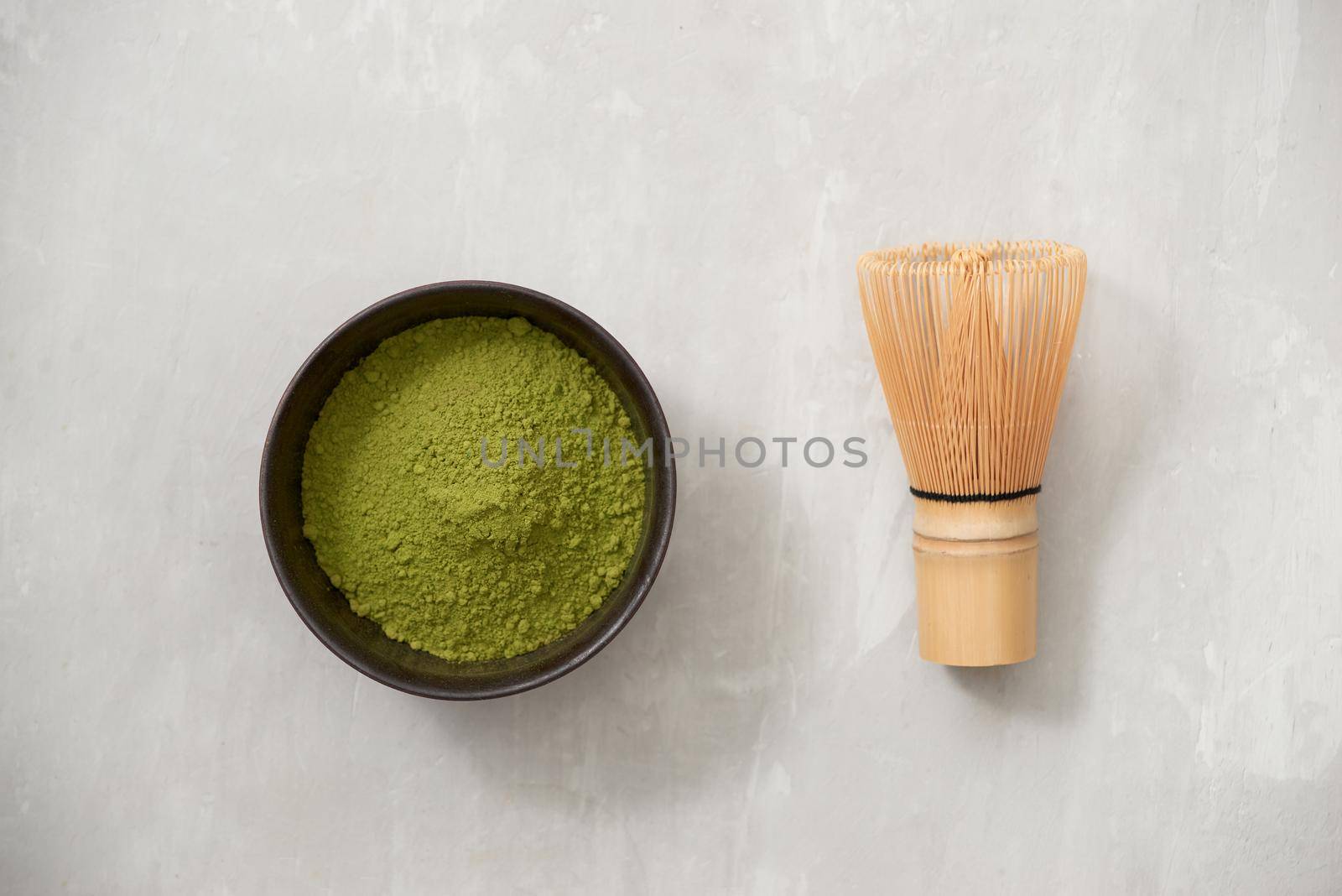 Matcha, green tea powder in black bowl with bamboo whisk on slate background. Top view. by makidotvn