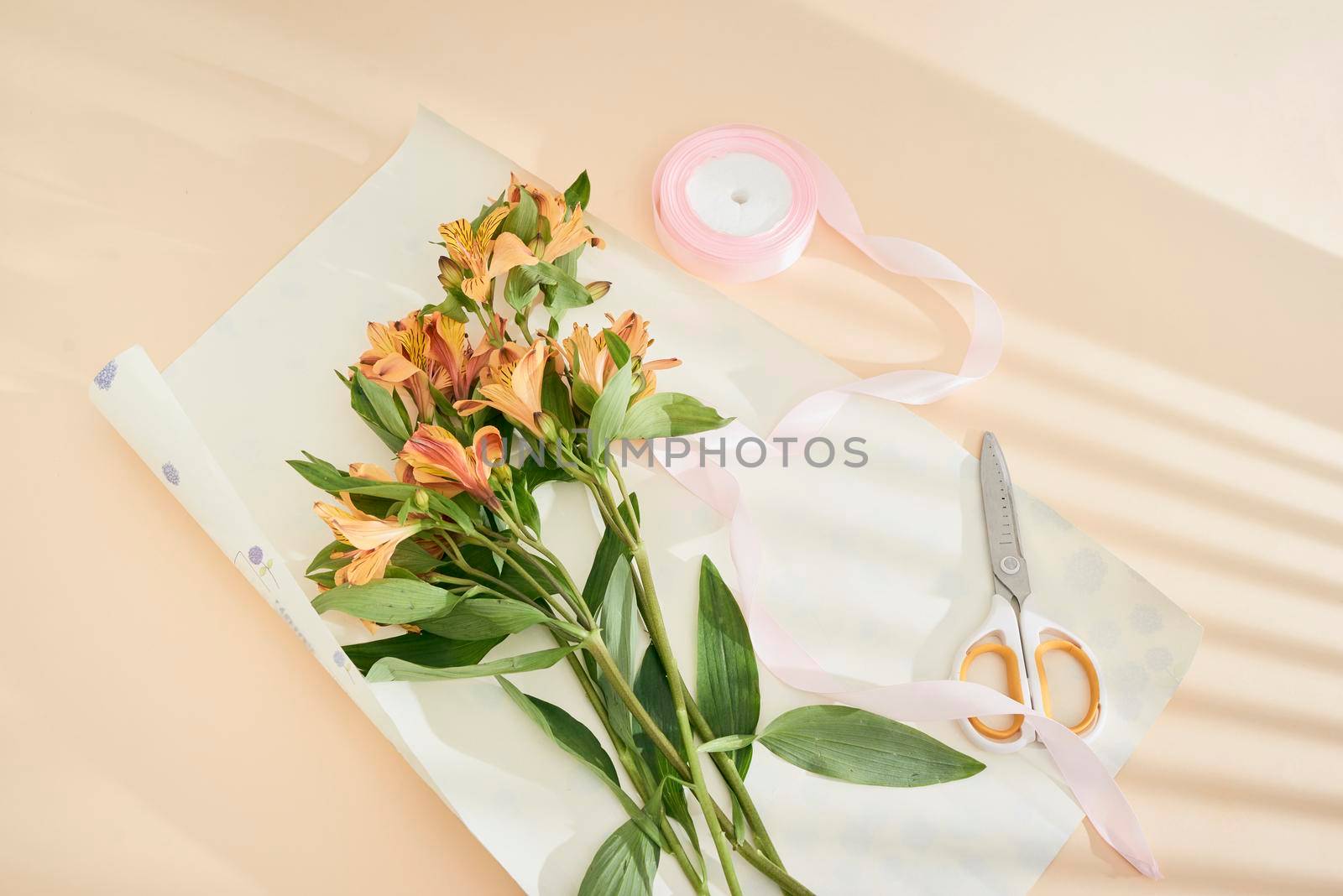 top view of beautiful orange flowers, scissors, ribbon and craft paper on paper surface by makidotvn