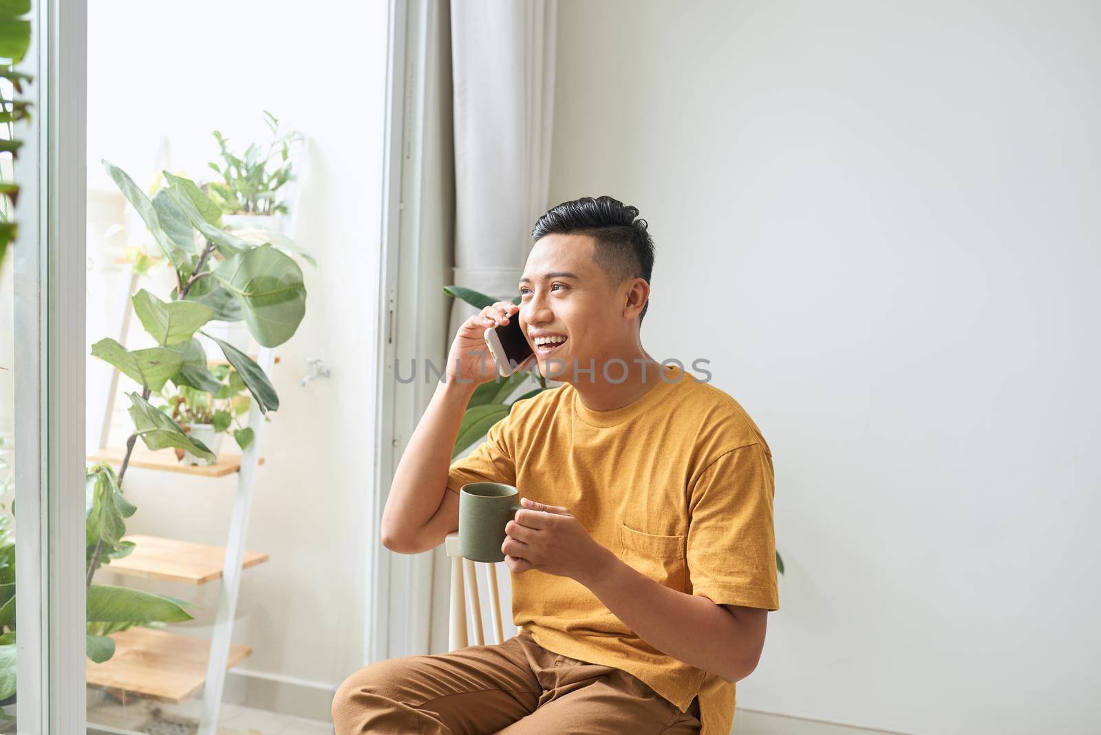 Young man wearing casual clothes talking on a mobile phone in the morning at a window