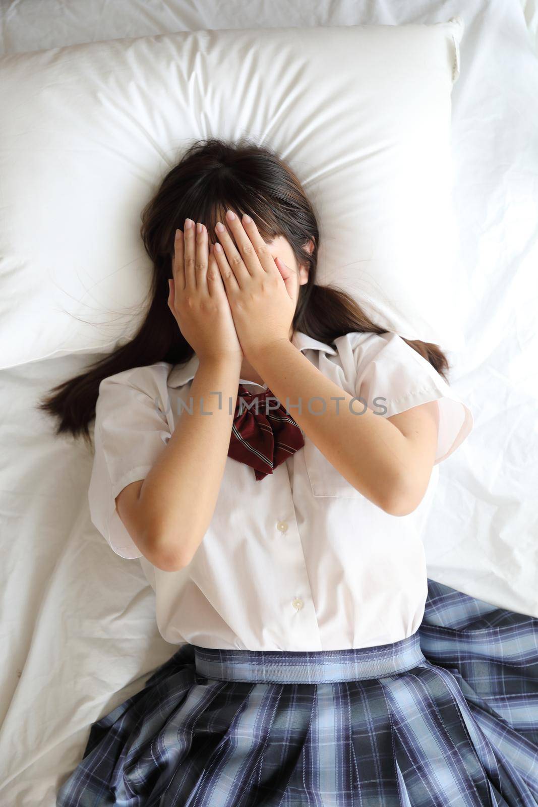 Portrait japanese school girl uniform sleep and look at camera in white tone bed room