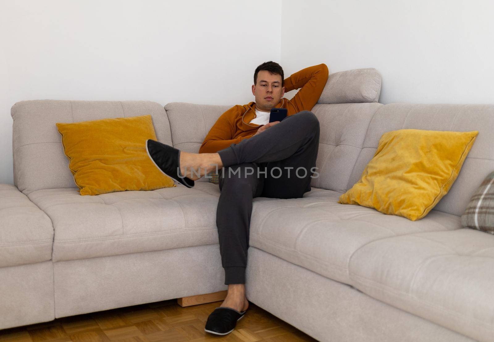 relaxed young man watching mobile phone on couch by Chechotkin