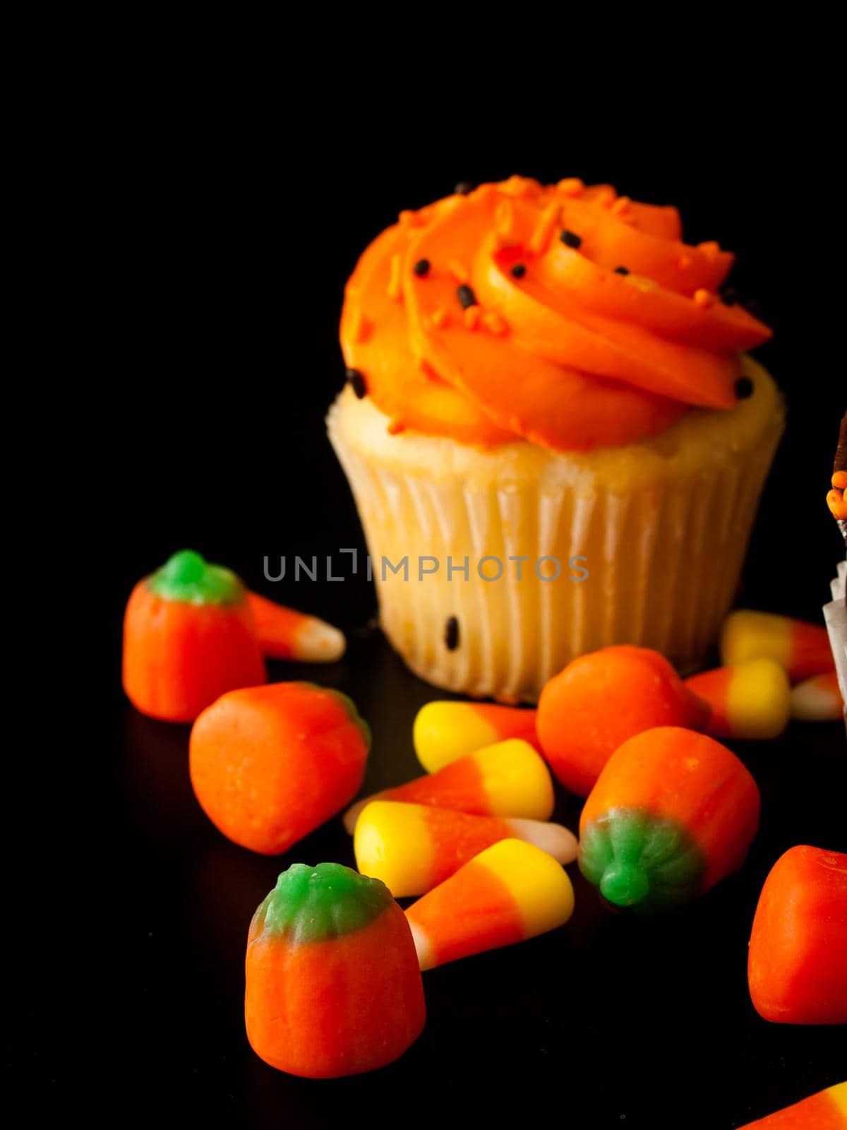 Halloween orange and black cupcakes with candy corn candies on black background.