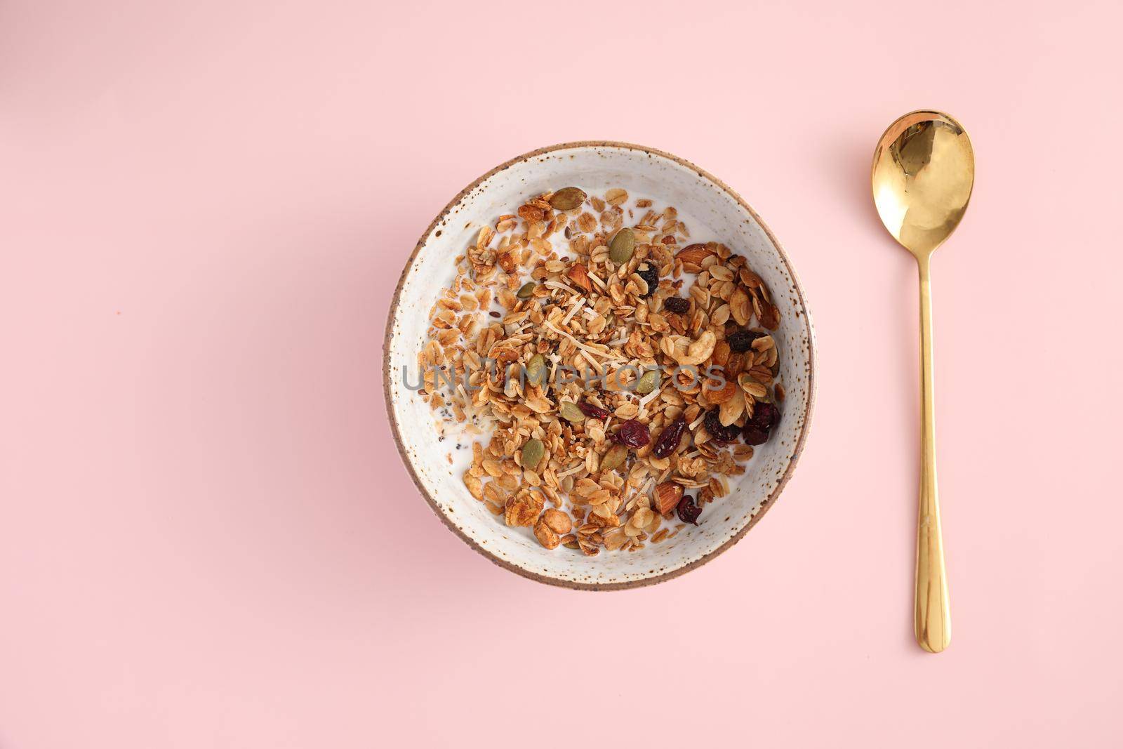 granola with milk with spoon isolated in pink background by piyato