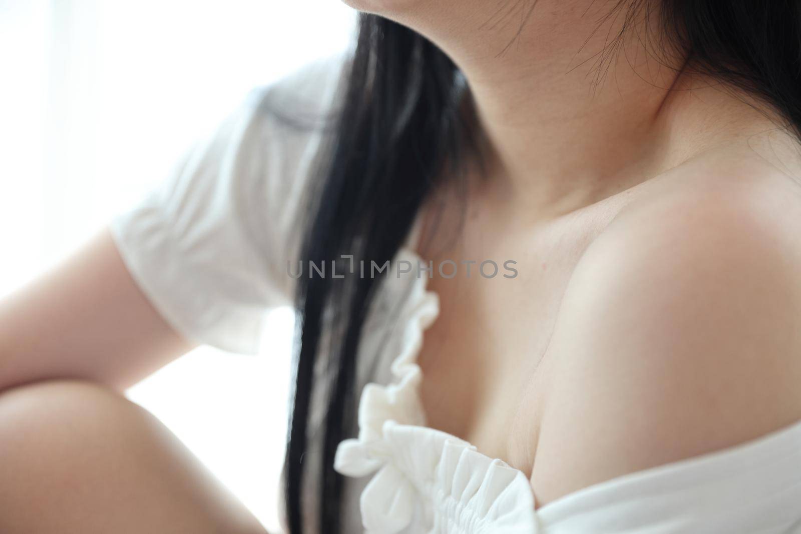 Close up of shoulder young Asian woman on bed relaxing in the morning light with white room by piyato